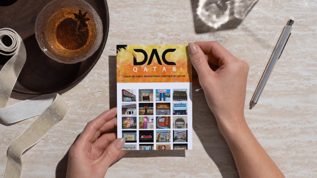 A person holding a DAC Qatar advertising brochure featuring the company’s name, tagline, and images of various advertising projects.