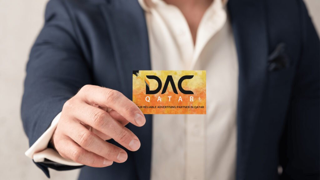 A person in a dark suit holding a DAC Qatar business card with a yellow-orange design and the tagline 'Your Reliable Advertising Partner in Qatar.
