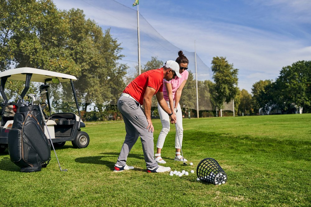 Young dark-haired woman in sunglasses learning to use a golf club assisted by her personal trainer